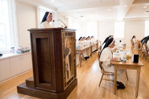 Sister reads from a spiritual book as the sisters eat supper